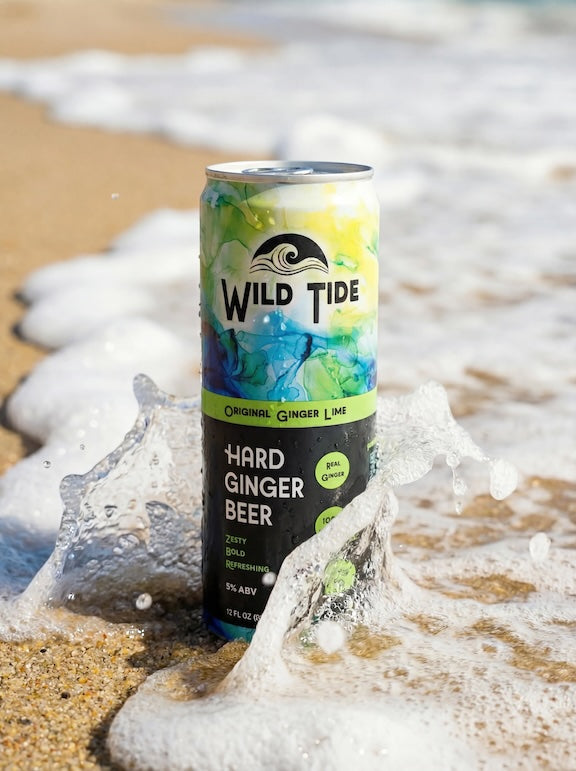 A can of Wild Tide Original Ginger Lime at the beach with a wave hitting it from the side.
