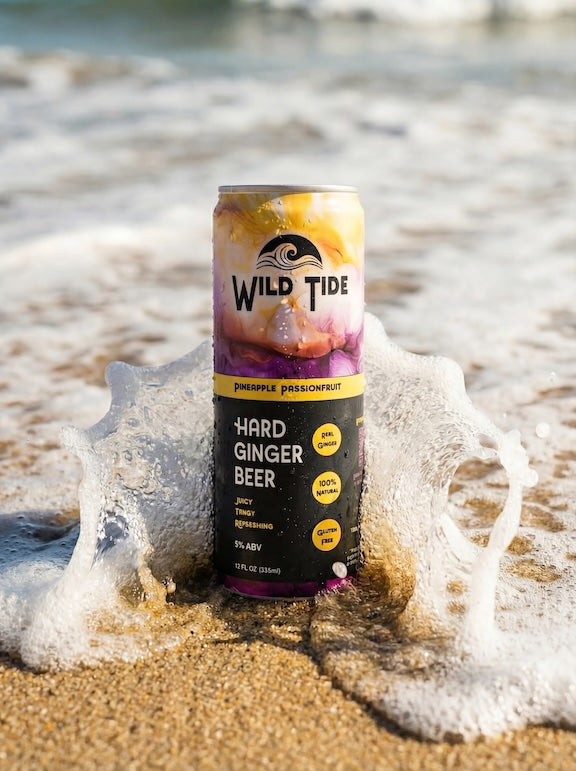 Wild Tide can of Pineapple Passionfruit on the beach with an ocean wave hitting it from the back.