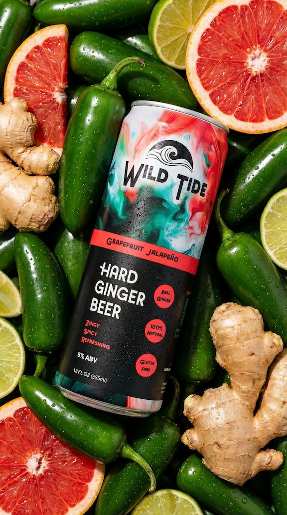 A can of Wild Tide Grapefruit Jalapeño ginger beer laying down in a pile of jalapeños, slices of grapefruit and lime, and pieces of ginger.