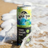 A can of Wild Tide Original Ginger Lime at the beach with a wave hitting it from the side.