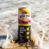 Wild Tide can of Pineapple Passionfruit on the beach with an ocean wave hitting it from the back.