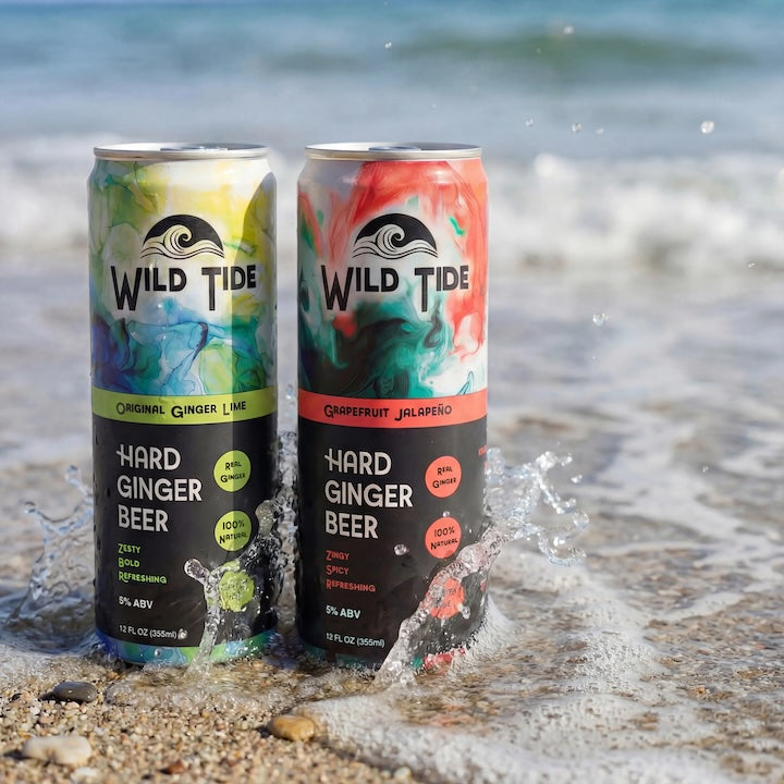 Two cans of Wild Tide Hard Ginger Beer on a beach with ocean waves.
