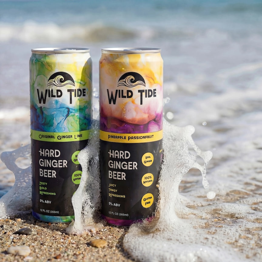 Two cans of Wild Tide Hard Ginger Beer on a beach with ocean waves.